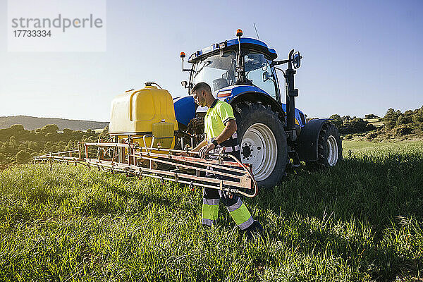 Young farmer adjusting crop sprayer on field on sunny day
