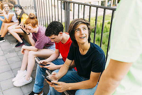 Junge mit Handy sitzt bei Freunden vor Geländer