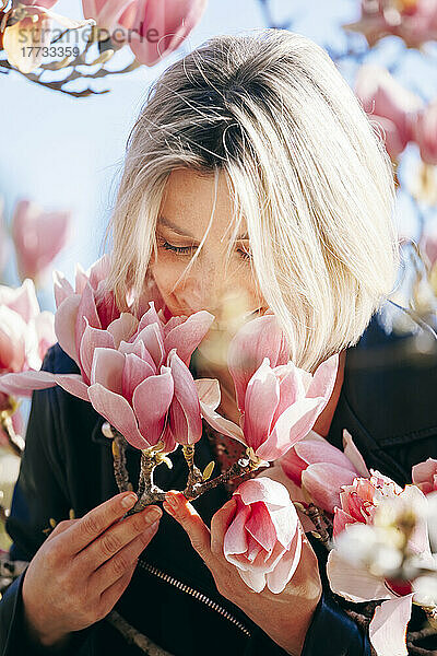 Lächelnde Frau  die an einem sonnigen Tag rosa Blumen riecht