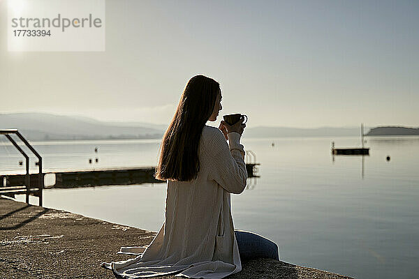 Frau trinkt an einem sonnigen Tag Kaffee am See