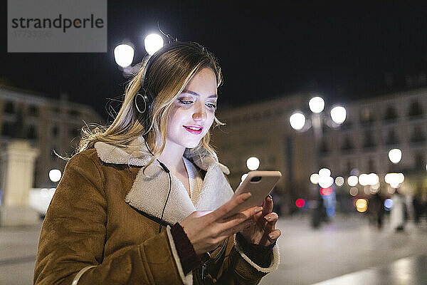 Frau mit Smartphone hört Musik über Kopfhörer in der Stadt