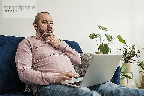 Nachdenklicher Geschäftsmann sitzt mit Laptop auf dem Sofa im Heimbüro