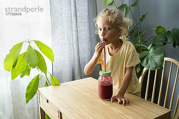 Mädchen trinkt zu Hause Smoothie durch Stroh