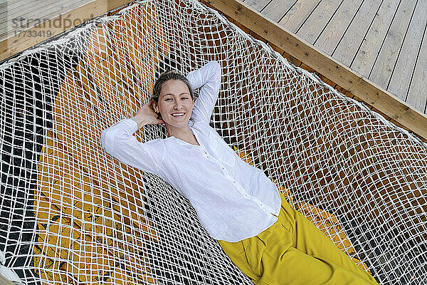 Smiling woman lying with hands behind head on hammock