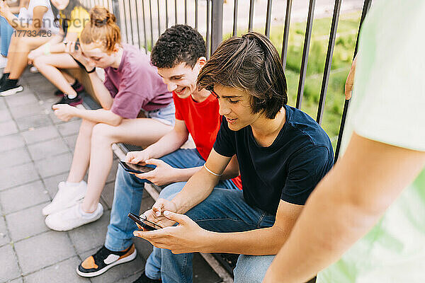 Junge benutzt Smartphone und sitzt neben Freunden