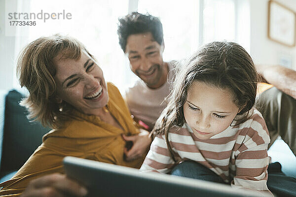 Glückliche Eltern schauen Tochter mit Tablet-PC an
