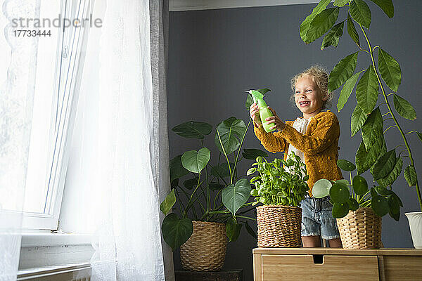 Glückliches Mädchen mit Sprühflasche  das zu Hause Pflanzen gießt