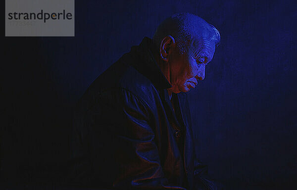 Deprimierter  einsamer älterer Mann  beleuchtet mit blauem Neonlicht vor schwarzem Hintergrund