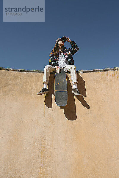 Junge Frau mit Skateboard sitzt an einem sonnigen Tag an der Sportrampe