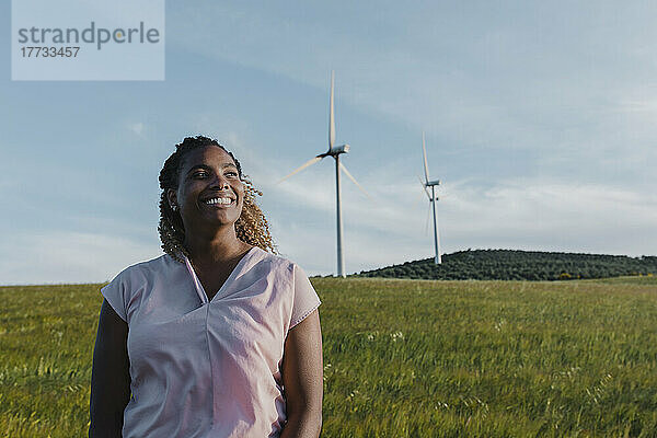 Glückliche Frau  die an einem sonnigen Tag vor einer Windkraftanlage steht