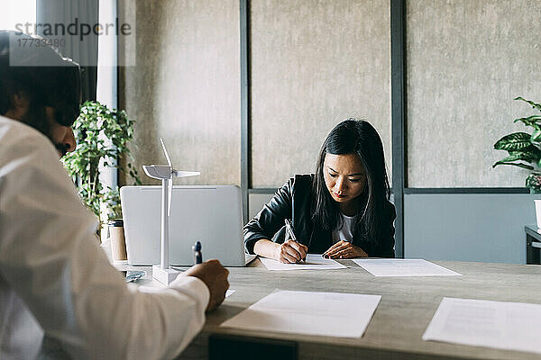 Geschäftskollegen schreiben am Schreibtisch im Büro auf Papierdokument
