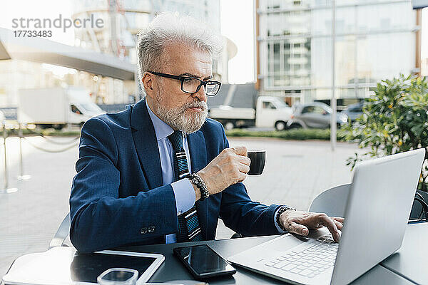Geschäftsmann mit Laptop trinkt Kaffee und sitzt im Straßencafé