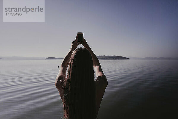 Frau fotografiert mit Handy am See