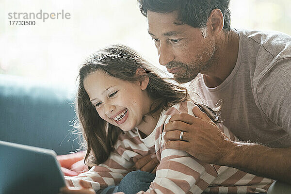 Reifer Mann mit fröhlicher Tochter  die zu Hause ein digitales Tablet nutzt