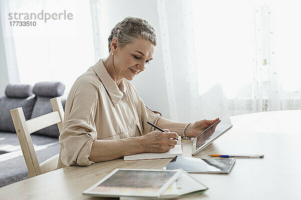 Frau nutzt digitales Tablet und macht sich zu Hause am Tisch Notizen