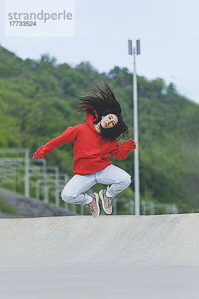 Frau mit zerzausten Haaren springt im Skateboardpark