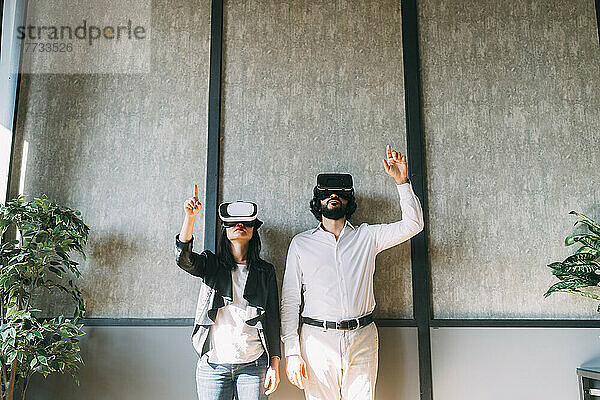 Geschäftskollegen mit VR-Brille gestikulieren vor der Wand