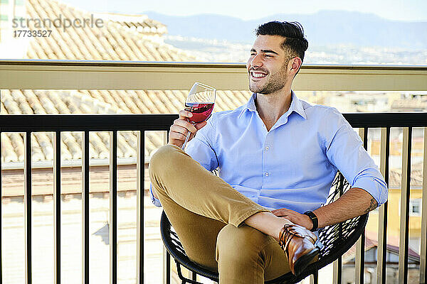 Glücklicher Mann mit Weinglas  der auf dem Balkon sitzt