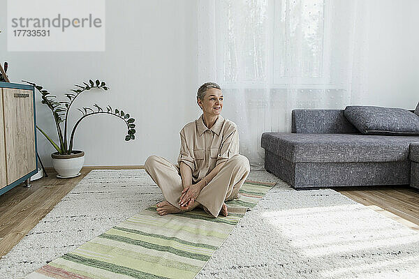 Reife Frau sitzt zu Hause auf dem Teppich