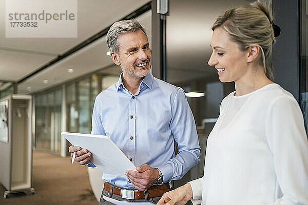Lächelnder Geschäftsmann mit digitalem Tablet und Geschäftsfrau im Gespräch im Büro