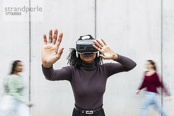 Smiling woman wearing virtual reality simulator gesturing in front of wall
