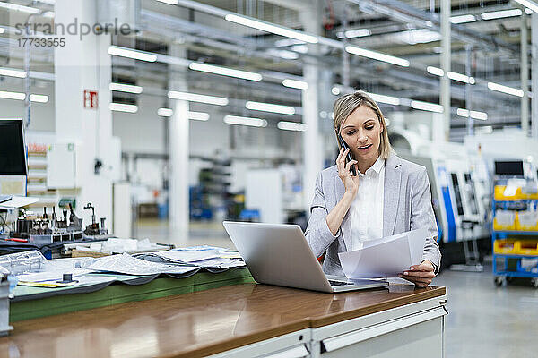 Geschäftsfrau mit Laptop am Telefon in der Fabrik