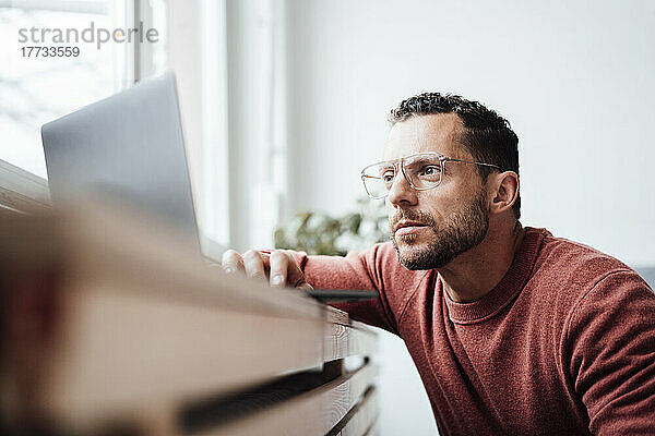 Freiberufler mit Brille arbeitet zu Hause am Laptop