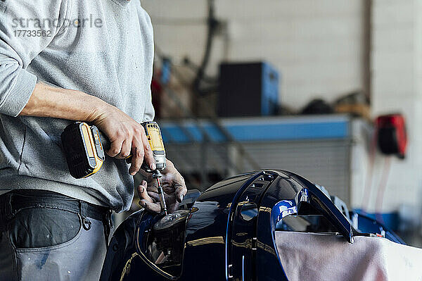 Hände eines Mechanikers reparieren Fahrzeugteile mit einem Elektroschrauber in der Werkstatt