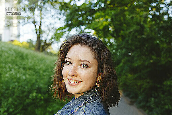 Lächelndes Teenager-Mädchen in Jeansjacke im Park