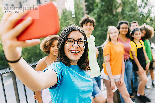 Fröhliches Mädchen mit Brille  das mit Freunden ein Selfie per Smartphone macht