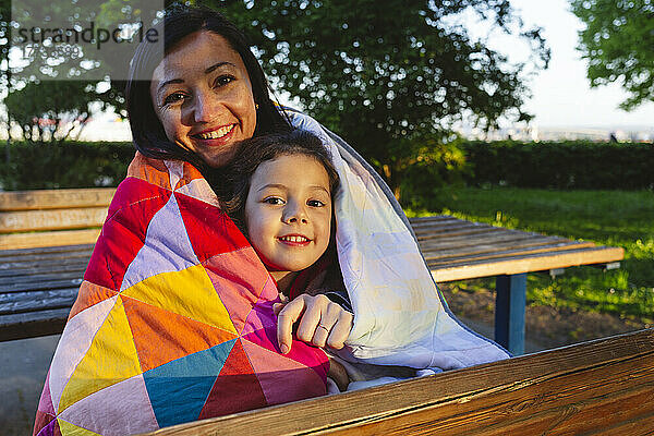 Glückliche Mutter und Tochter im Park in eine Steppdecke gehüllt