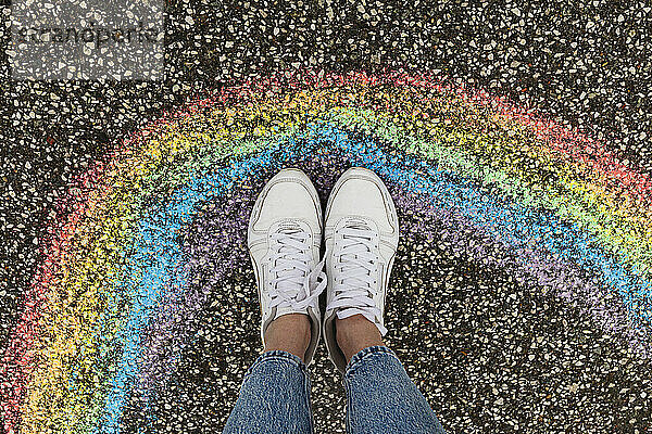 Woman wearing white shoes standing by rainbow drawing on road