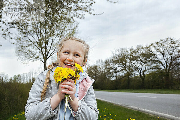 Glückliches Mädchen hält einen Strauß Löwenzahnblüten in der Nähe der Straße