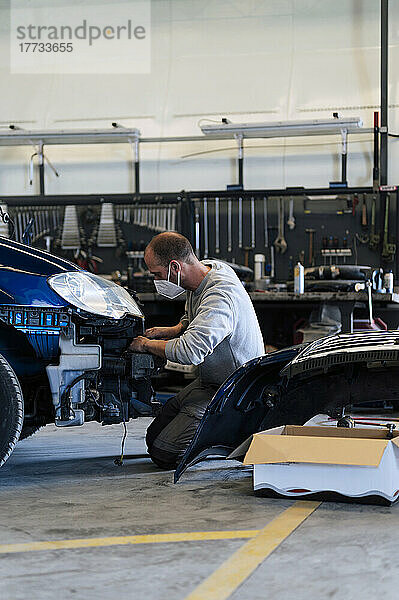 Automechaniker kniet und repariert Auto in Garage