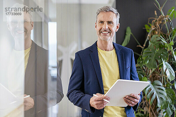 Smiling businessman holding digital tablet in office