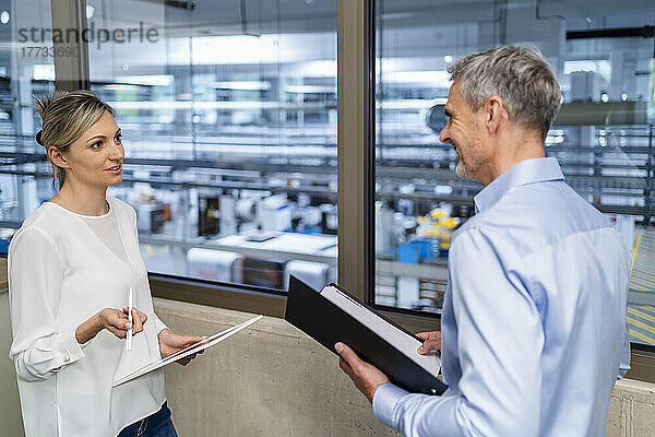 Geschäftsmann mit Klemmbrett und Geschäftsfrau mit digitalem Tablet unterhalten sich im Fabrikbüro