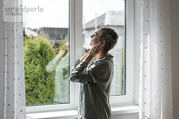 Reife Frau steht zu Hause am Fenster