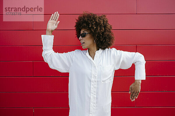 Afro-junge Frau mit Sonnenbrille tanzt vor roter Wand