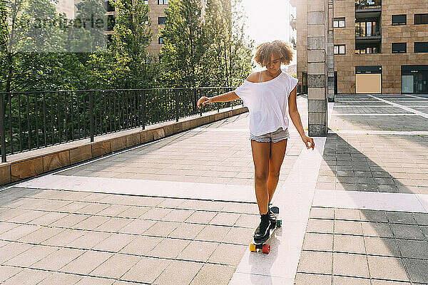Mädchen mit Afro-Frisur beim Skateboarden an einem sonnigen Tag