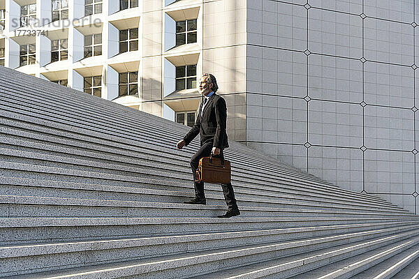 Reifer Geschäftsmann mit Tasche bewegt sich die Treppe hinauf