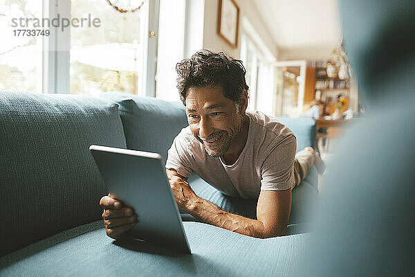 Glücklicher Mann benutzt Tablet-PC auf dem Sofa zu Hause