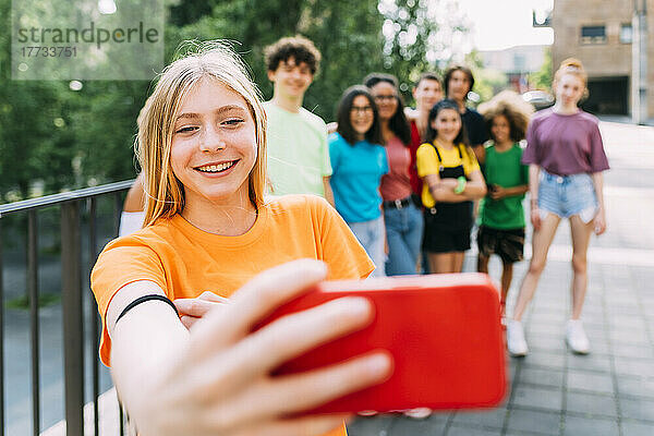 Glückliches blondes Mädchen  das mit Freunden ein Selfie per Handy macht