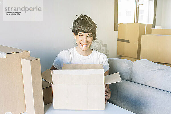Glückliche Frau mit Kartons  die zu Hause im Wohnzimmer sitzt