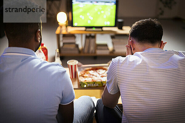 Young football fans watching soccer match together at home
