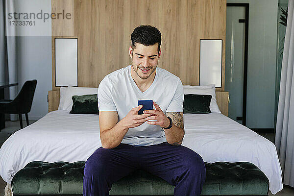 Junger Mann benutzt Smartphone im Schlafzimmer zu Hause