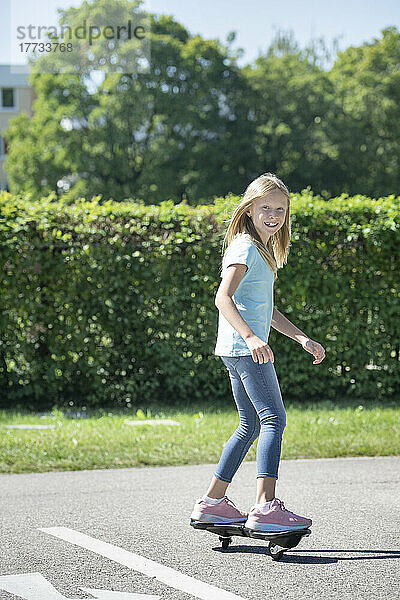 Lächelndes blondes Mädchen  das auf der Verkehrsstrecke Skateboard fährt