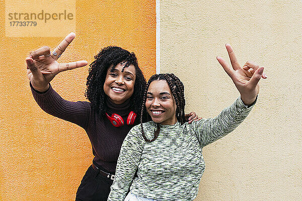 Smiling women gesturing peace sign in front of wall
