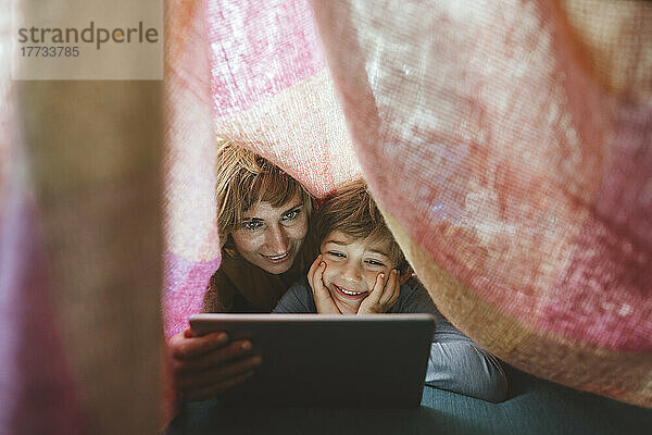 Glückliche Mutter und Sohn nutzen Tablet-PC unter der Decke