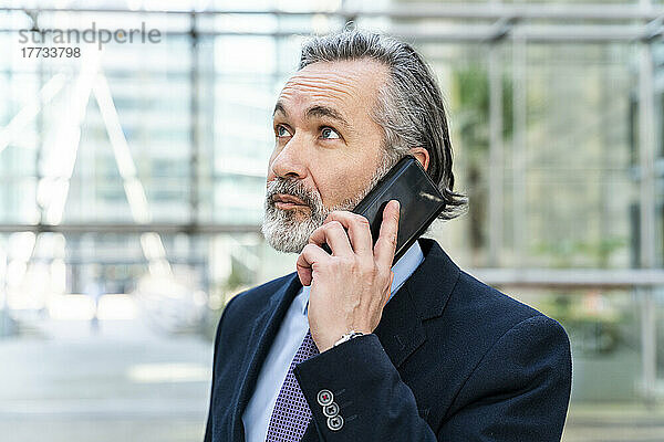 Lächelnder Geschäftsmann mit grauen Haaren  der auf dem Smartphone spricht