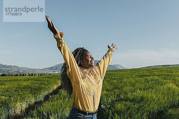 Happy young woman with arms raised in meadow